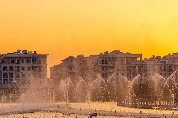 stock image Big fountains on the artificial pond, illuminated by sunlight at sunset in Tashkent city park at summertime evening.