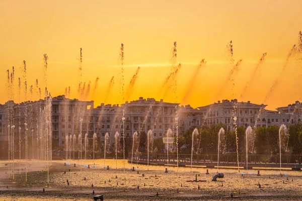 stock image Big fountains on the artificial pond, illuminated by sunlight at sunset in Tashkent city park at summertime evening.