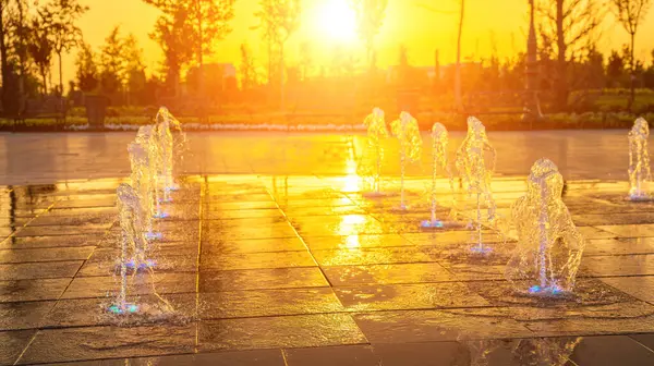 人行道上的小喷泉 夏天的日落或日出时被阳光照亮 — 图库照片
