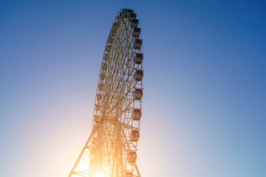 Günbatımında yüksek dönme dolap ya da Özbekistan 'ın Taşkent kentindeki Navruz lunaparkında mavi gökyüzü arka planlı gün doğumu.