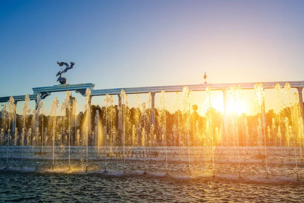 乌兹别克斯坦塔什干独立广场的纪念碑和一排排的喷泉在日落或日出时被阳光照亮 — 图库照片