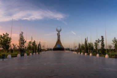 UZBEKISTAN, TASHKENT - 15 Eylül 2023: Yeni Özbekistan parkında dramatik bir kliodi gökyüzü ile alacakaranlıkta bir Humo kuşuyla birlikte bir çelik şeklinde Bağımsızlık Anıtı.