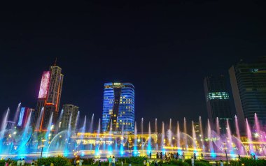 Özbekistan, Taşkent - 27 Eylül 2023: Taşkent Şehir Parkı 'nda gece vakti bir tırpan ve Hilton Otel binasının zeminine karşı lazer aydınlatma ve hafif müzik içeren bir çeşme.