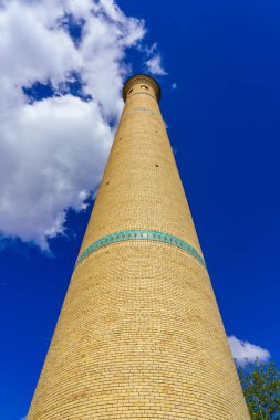 Gündüz vakti bulutlu bir gökyüzüne karşı tuğladan bir caminin minaresi.