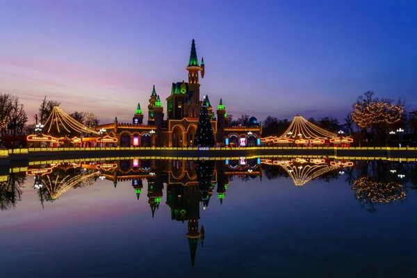 stock image Tashkent, Uzbekistan - December 11, 2023: Magic City amusement park on a late evening reflected in a water with decorations.