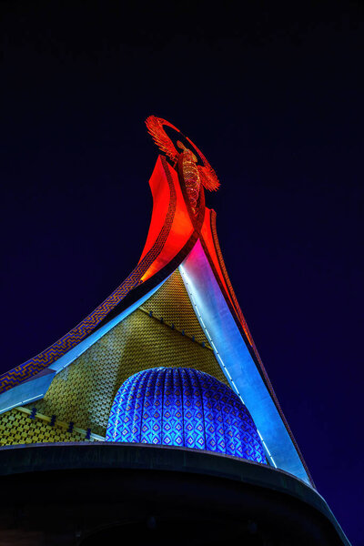 Uzbekistan, Tashkent - December 11, 2023: Illuminated monument of independence in the form of a stele with a Humo bird in the New Yangi Uzbekistan park at nighttime.