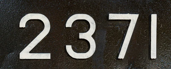 Weathered numbers two, three, seven; one; 2371 or 2, 3, 7, 1 painted white on a piece of black metal. Abstarct numeral background for design.