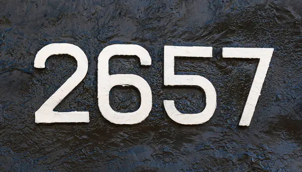 Weathered numbers two, six, fiveseven; one; 2657 or 2, 6, 5, 7 painted white on a piece of black metal. Abstarct numeral background for design.