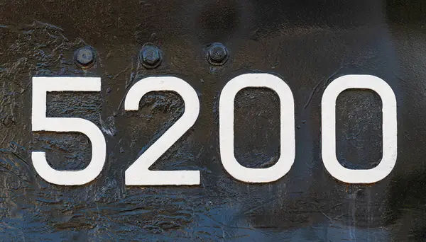 Weathered numbers zero, two, five, 5200, or 5, 2, 0 painted white on a piece of black metal. Abstarct numeral background for design.