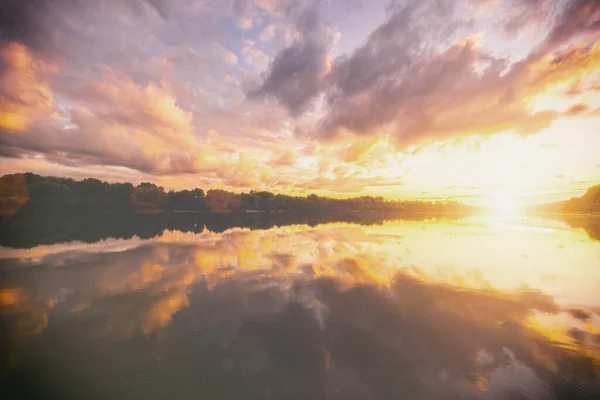 Sunrise or sunset on a lake or river with dramatic cloudy sky reflection in the water in spring. Springtime rural landscape. Aesthetics of vintage film.