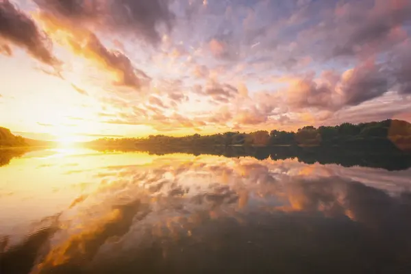 Sunrise or sunset on a lake or river with dramatic cloudy sky reflection in the water in spring. Springtime rural landscape. Aesthetics of vintage film.