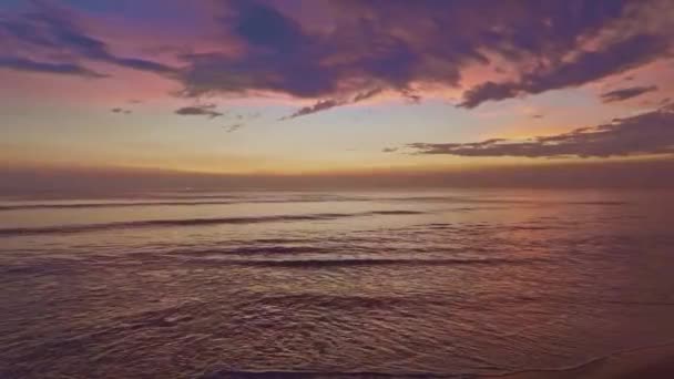 砂浜の上にカラフルな光の夕日に向かって転がり泡立つ波の波がクラッシュするビーチでの黄金の夕日 美しい景色の夕日や海の上の日の出 ビーチでクラッシュする海の波 カラフルな空 — ストック動画