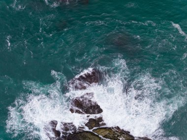 Deniz kıyısındaki kayalara çarpan dalgalar, arka plandaki deniz yüzeyi dalgaları