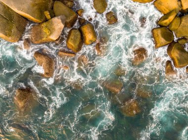 Deniz kıyısındaki kayalara çarpan dalgalar, arka plandaki deniz yüzeyi dalgaları