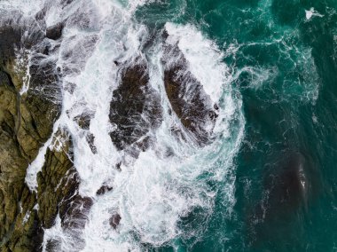 Deniz kıyısındaki kayalara çarpan dalgalar, arka plandaki deniz yüzeyi dalgaları