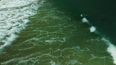 Deniz çarpan dalgaların havadan görünüşü kumsaldaki beyaz köpüklü dalgalar, plaj yüzeyinin üst görünüşü arka plan inanılmaz renkli sahil denizi harika kum arka plan.