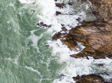 Deniz kıyısındaki kayalara çarpan dalgalar, arka plandaki deniz yüzeyi dalgaları