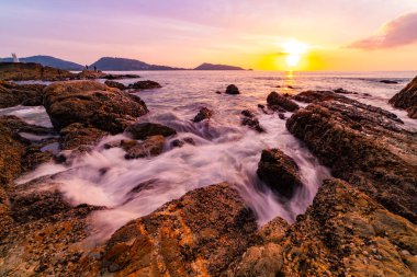 Gün batımında ya da gündoğumunda sahile vuran kaya ve dalgalarla dramatik gökyüzünün uzun pozlama görüntüsü