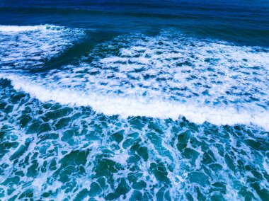 Üst manzara dalgaları kumlu sahile çarpıyor, sahilin deniz manzarası arka planında