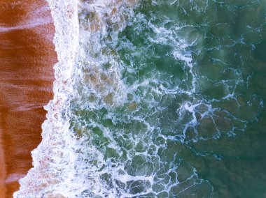 Üst manzara dalgaları kumlu sahile çarpıyor, sahilin deniz manzarası arka planında