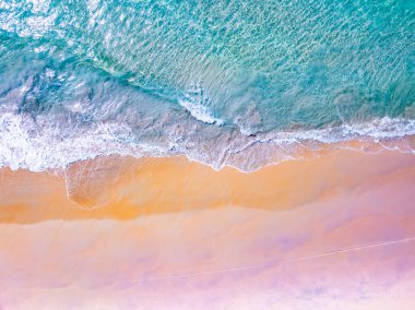 Üst manzara dalgaları kumlu sahile çarpıyor, sahilin deniz manzarası arka planında