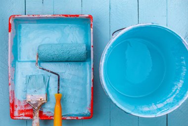Renk tepsisinde boya fırçası ve boya kovası, mavi ahşap arka planda beyaz eldiven.