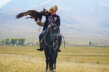 Kırgız göçebe binici bir kartalı elinde tutuyor ve bir atın üzerinde oturuyor.