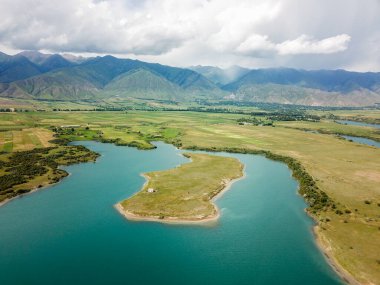 Güneşli bahar günü, arka planda su ve dağlarla çevrili ıssız bir adada otlayan at sürüsü manzarası.
