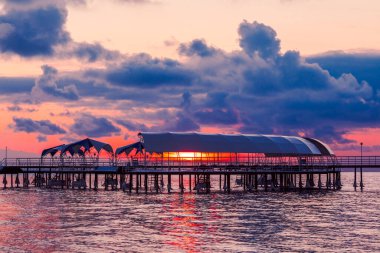 Okyanusun üzerinde devasa bir bulut ve iskelenin siluetiyle inanılmaz renkli günbatımının yakın çekimi