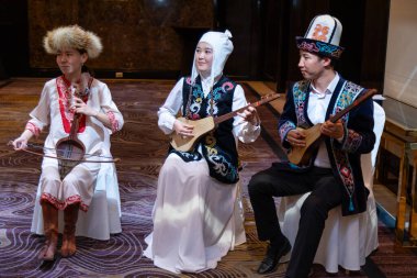 Bishkek, Kyrgyzstan - June 18, 2022: Kyrgyz musicians wearing national dresses playing on a national instrument called Kyl Kiak and Komuz clipart