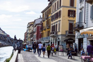 Milan, Italy - March 14, 2023: Sunny day on Milan's canal walkway, lined with elegant multi-colored buildings and vibrant street cafs, inviting passersby and diners  clipart