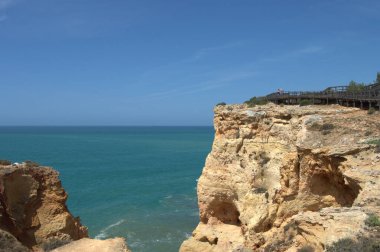 Carvoeiro, Portekiz - 13 Mayıs 2022: Carvoeiro, Portekiz 'deki Carvoeiro Boardwalk manzaralı bir manzara, kayalıklar boyunca beyaz yetişkinler ve yaşlılarla güneşli bir günün keyfini çıkaran yollar