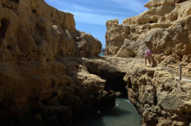 Carvoeiro, Portugal - May 13, 2022: Visitors at the Carvoeiro Boardwalk navigate the rugged rocky cliffs, with a couple of Caucasian adults seen at the top of the rock formation, enjoying the scenic views clipart