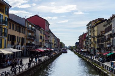 Milan, İtalya - 14 Mart 2023: Milano kanal geçidinde güneşli bir gün, şık renkli binalar ve hareketli sokak kafeleriyle dolu, yoldan geçenleri ve lokantaları davet eden  