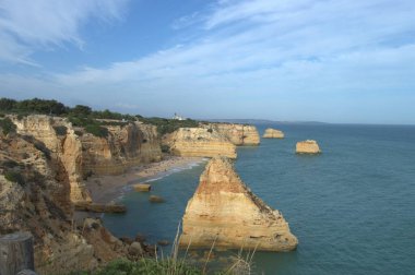 Carvoeiro, Portekiz - 13 Mayıs 2022: Praia de Carvoeiro 'daki kayalık plajda büyüleyici kayalıklar ve manzaranın keyfini çıkaran turistlerin bulunduğu açık bir okyanus manzarası yer almaktadır.