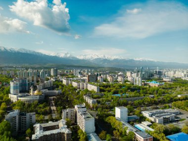 Güneşli bahar gününde, arka planda karla kaplı dağlarla Almaty şehrinin hava manzarası.