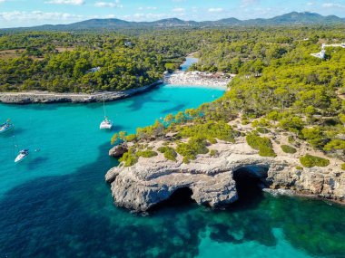 İspanya 'nın Mallorca Adası' ndaki Cala Llombards (Santanyi) plaj koyunda güneşli yaz günlerinde yüzen teknelerin hava görüntüsü