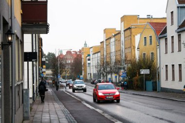 Malmö, İsveç - 12 Ocak 2023: Yayaların ve araçların renkli binalarla dolu bir cadde boyunca ilerlediği bir İsveç şehrinde tipik bir iş günü sahnesi