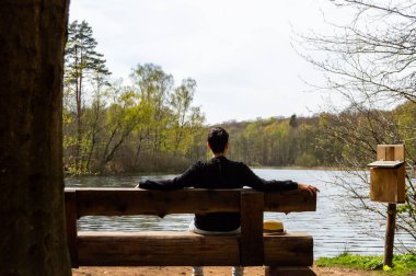 İsveç 'teki Soderasen Ulusal Parkı' nda ahşap bir bankta oturan ve göl manzarasının keyfini çıkaran bir adam.