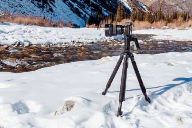 Kırgızistan 'daki Ala-Archa Doğa Parkı' nda akan dağ nehrinin fotoğrafını çeken tripodun üzerindeki dijital kamera.