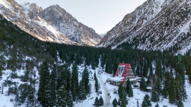 Kırgızistan 'daki Ala-Archa Doğa Parkı' nda kışın karla kaplı dağlar ve otel manzaralı köknar ağaçları.