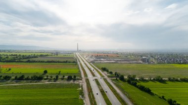 Bereketli yeşil tarlaların ve canlı haşhaş tarlalarının havadan görünüşü bir otoyol ile kesişiyor, açık bir gökyüzünün altında inşaat yapılıyor.
