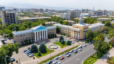 Bişkek, Kırgızistan - 30 Temmuz 2024: Bishkek Belediye Binası ve çevresini çevreleyen yeşillik, binalar ve park halindeki arabalarla detaylı hava manzarası