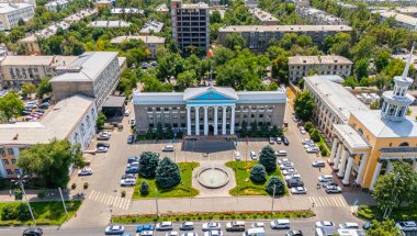 Bişkek, Kırgızistan - 30 Temmuz 2024: Güneşli bir günde bitişik binalar, yeşillikler ve hareketli caddelerle Bishkek Belediye Binası panoramik hava manzarası
