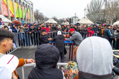 Bişkek, Kırgızistan - 21 Mart 2024: Kırgız erkekler Bişkek şehrinin merkez meydanında Nowruz bayramı sırasında bilek güreşi. Nowrus, ilkbaharın ve yeni yılın gelişinin bayramıdır.