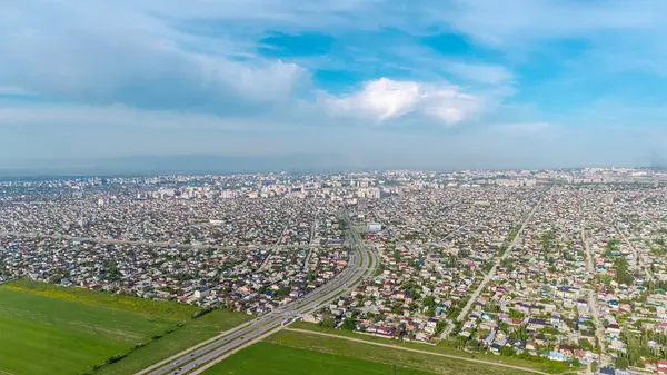 stock image Aerial view of Bishkek city suburbs and highway entrance with a vast expanse of residential houses and green fields under a partly cloudy sky