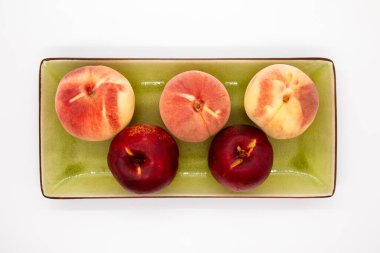 Olgun organik şeftaliler yeşil tabakta beyaz arka planda