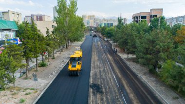 Bishkek, Kyrgyzstan - August 14, 2024: Aerial view of road construction with yellow asphalt rollers laying new pavement clipart