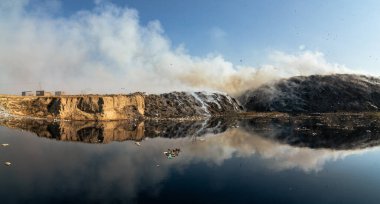 Yanan çöp yığınlarıyla panoramik manzara ve kirlenmiş zehirli gölet