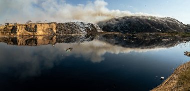 Yanan çöp yığınlarıyla panoramik manzara ve kirlenmiş zehirli gölet